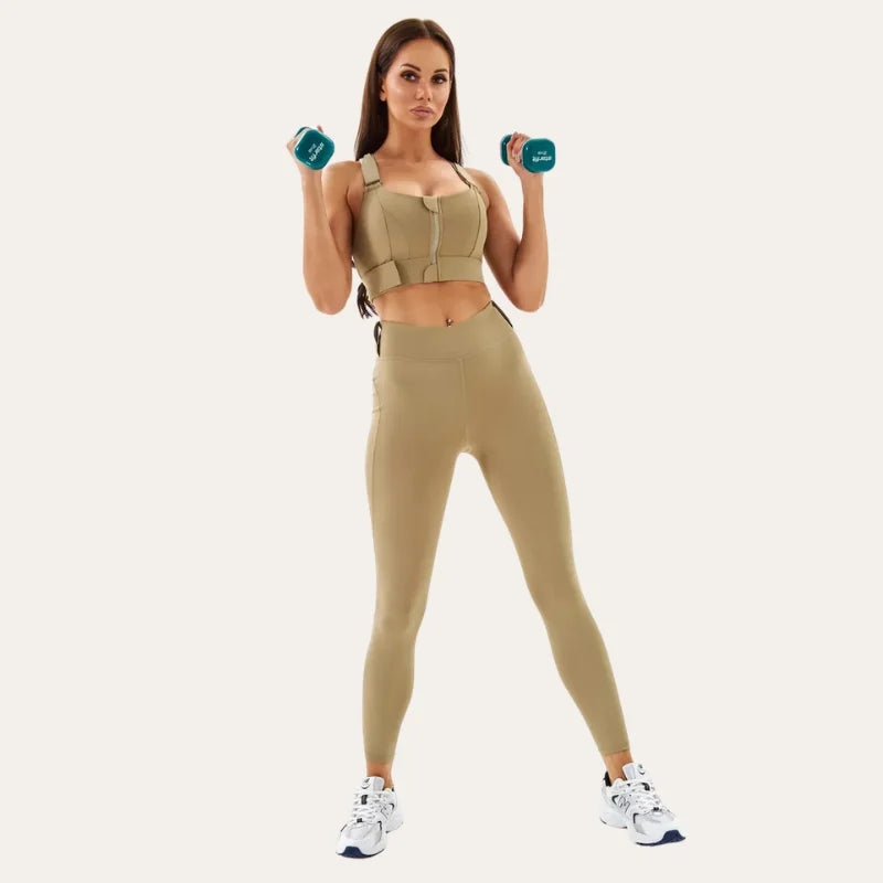 Modelo em corpo inteiro vestindo soutien desportivo Alba savana com leggings desportivas da mesma cor, segurando halteres em postura de treino