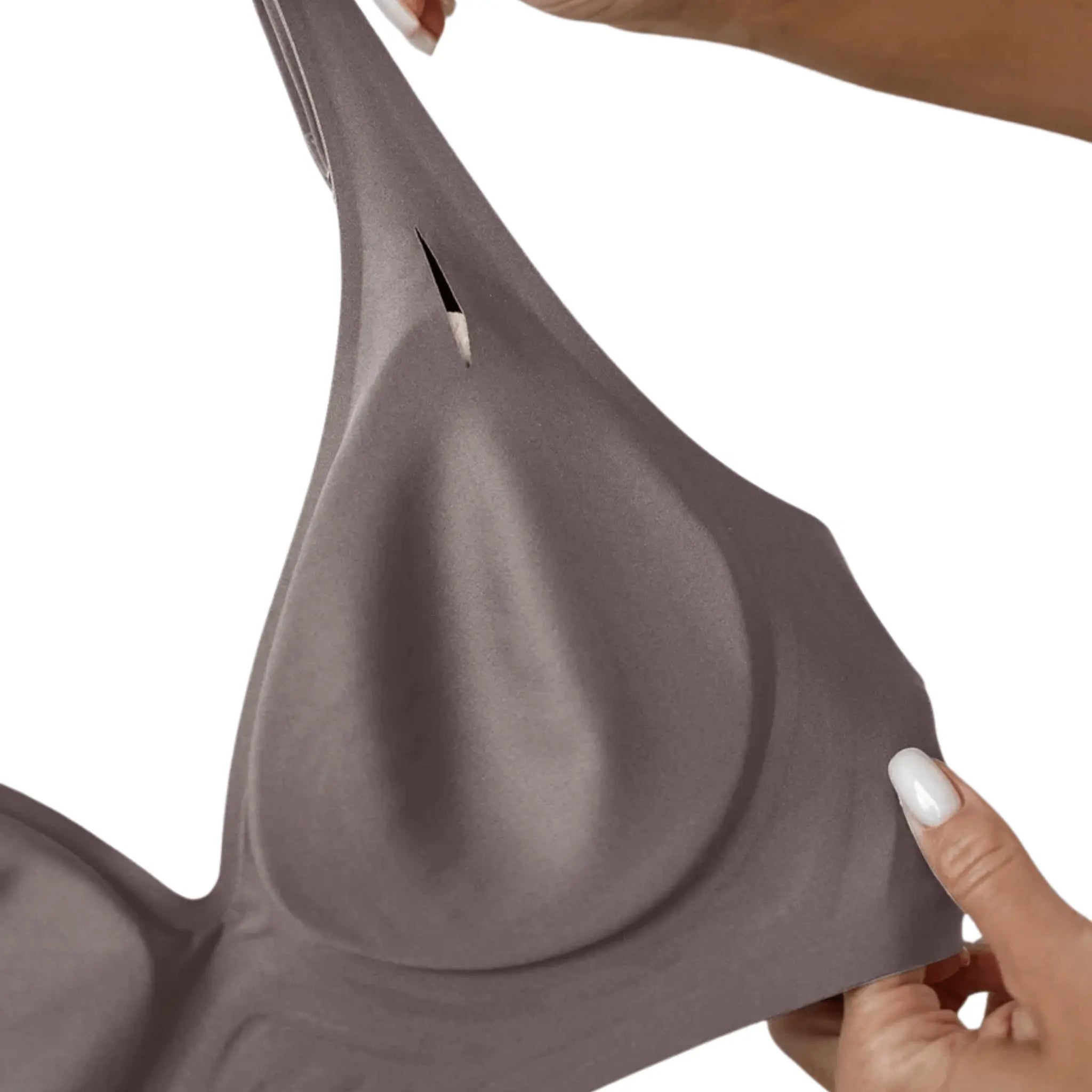 Mãos segurando sutiã nude pelo lado de dentro, mostrando o bojo macio e o corte triangular.